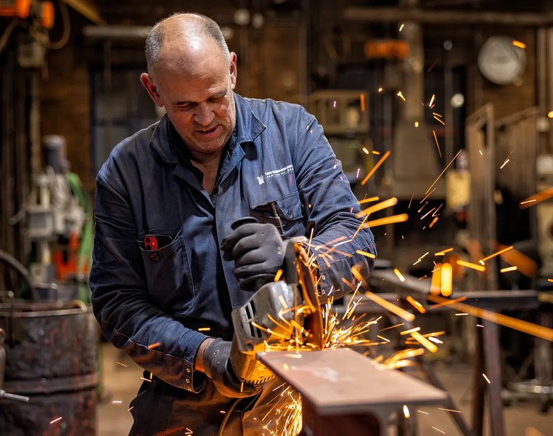 Hendrik-Jan van den Bergh slijpt een stalen profiel in de werkplaats; vonken spatten op
